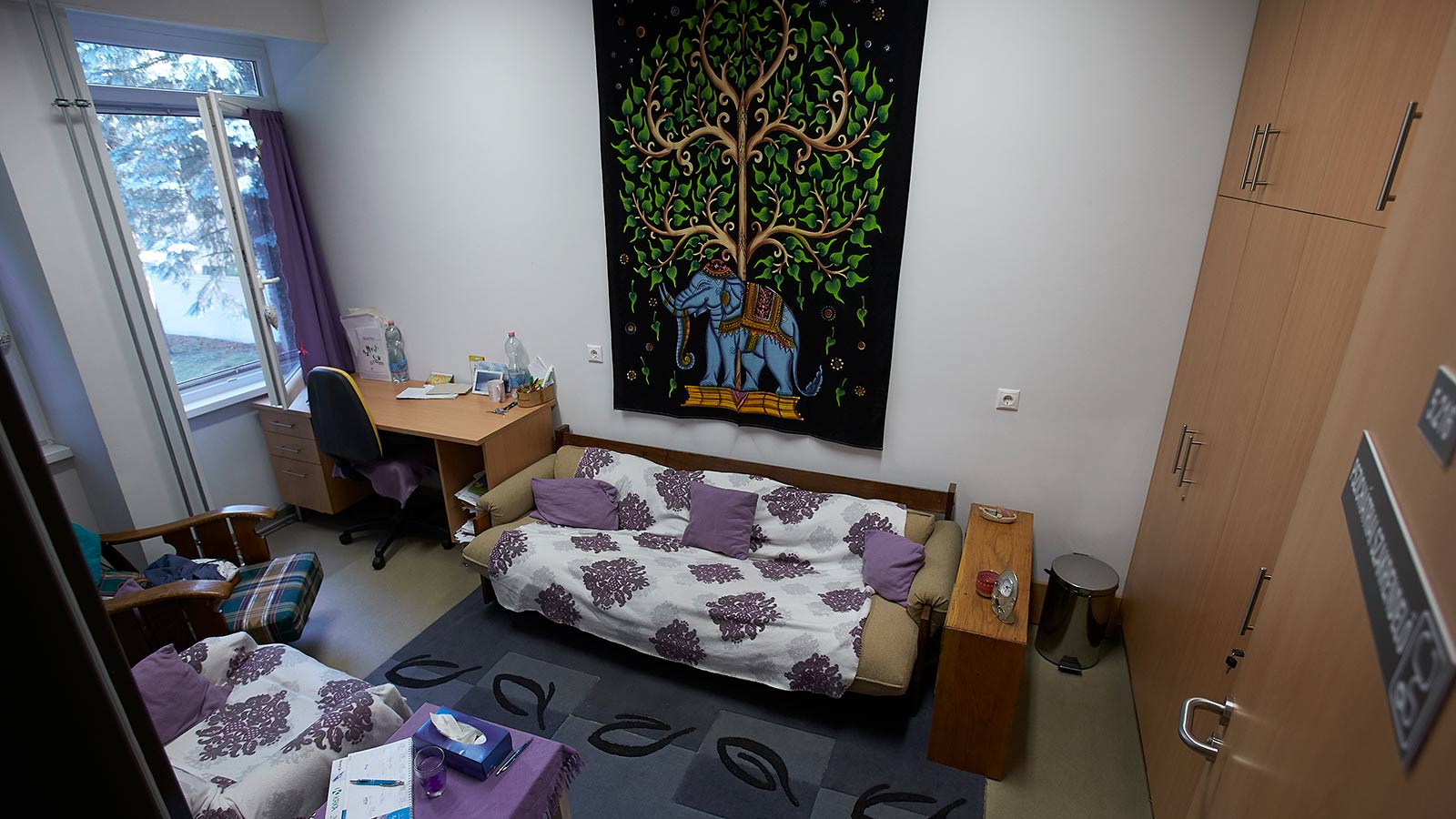 Pszichiátriai szakrendelő íróasztallal, kanapéval, fotellel, elefántos szőttes a falon